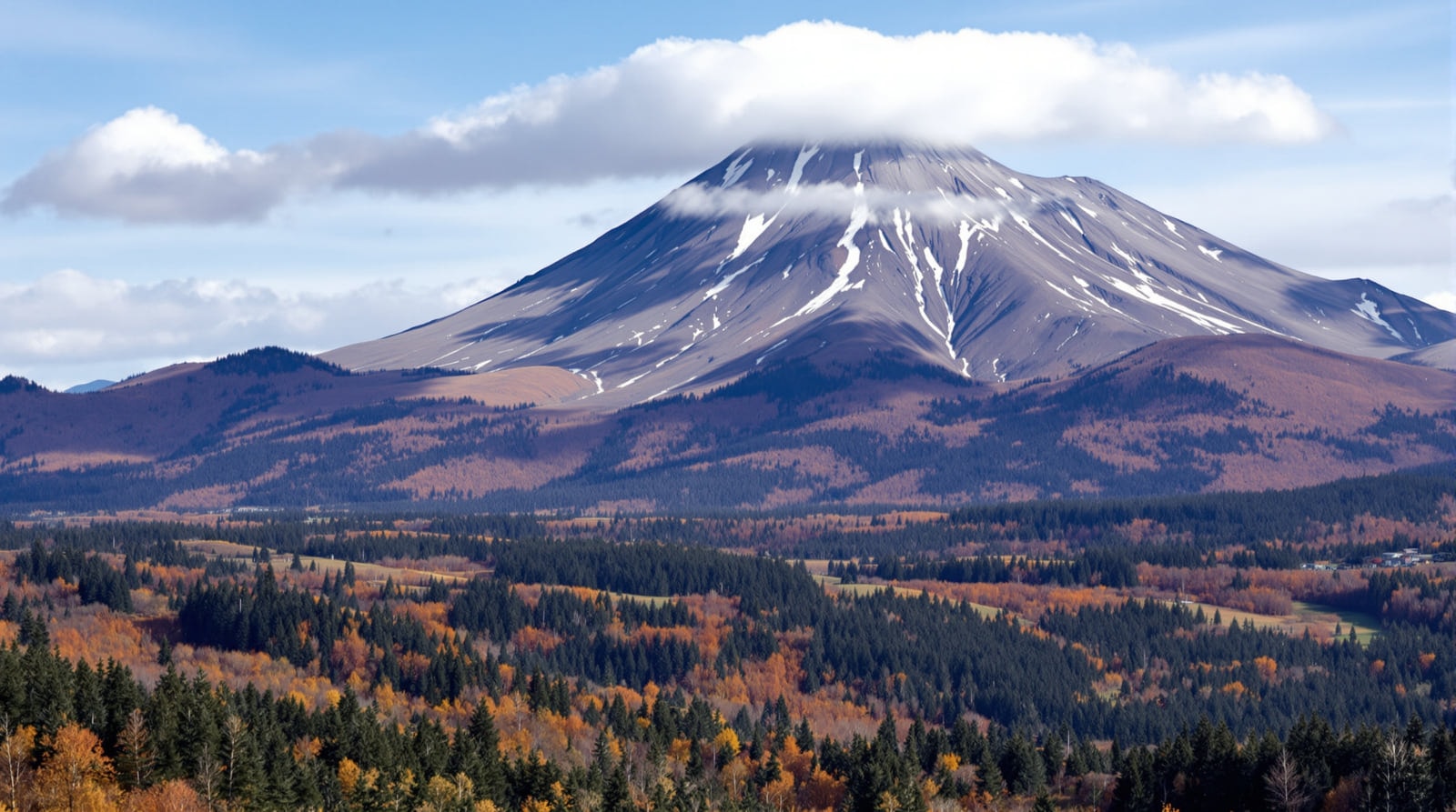 A distinctive undeveloped double-summited mountain peak seen across a broad forested valley in autumn