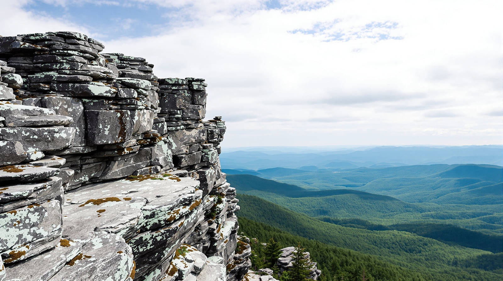 Bare rocky summit of a Vermont mountain with lichen-covered ledges and a panoramic view over forested ridges